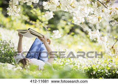 Woman reading book in grass under tree with white blossoms View Large Photo Image Stock Image - Woman reading book in grass under tree with white blossoms. Fotosearch