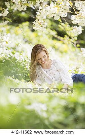 Woman reading book in grass under tree with white blossoms View Large Photo Image Stock Image - Woman reading book in grass under tree with white blossoms. Fotosearch