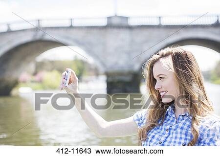Stock Image - Woman taking self-portrait along river. Fotosearch