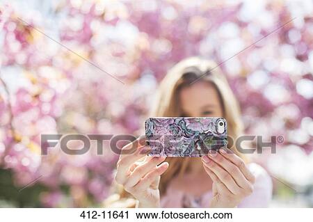 Stock Image - Woman taking self-portrait with cell phone outdoors. Fotosearch