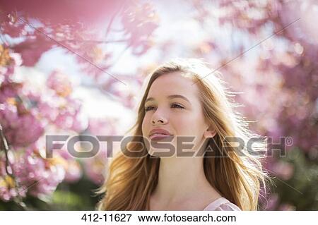 Stock Photo - Woman walking under tree with pink blossoms. Fotosearch
