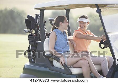 Stock Image - Women driving cart on golf course. Fotosearch