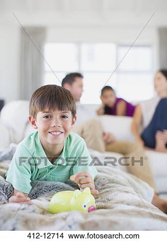 Picture - Boy counting change in piggy bank on sofa in living room. Fotosearch