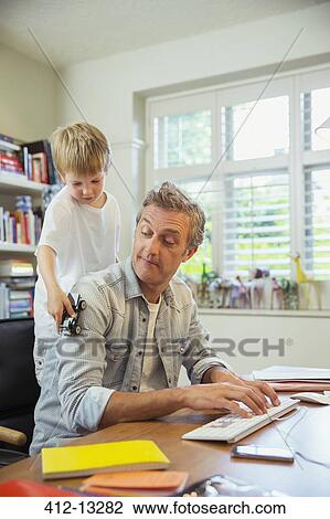 Boy distracting father at work in home office View Large Photo Image Stock Image - Boy distracting father at work in home office. Fotosearch