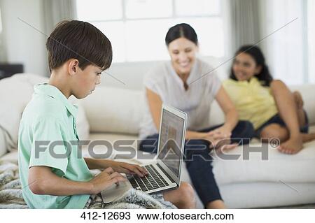 Boy using laptop on sofa in living room View Large Photo Image Stock Image - Boy using laptop on sofa in living room. Fotosearch