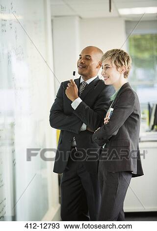 Stock Image - Business people looking at whiteboard in office. Fotosearch