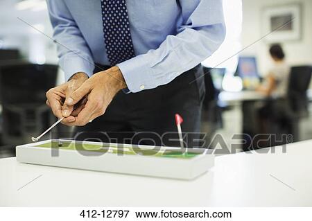 Businessman playing with toy golf set in office View Large Photo Image Stock Photo - Businessman playing with toy golf set in office. Fotosearch