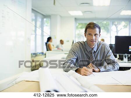 Businessman reading blueprints in office View Large Photo Image Stock Photography - Businessman reading blueprints in office. Fotosearch