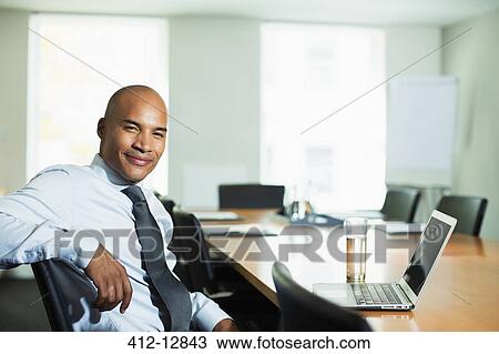 Stock Image - Businessman smiling at conference table. Fotosearch
