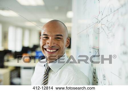 Businessman smiling at whiteboard in office View Large Photo Image Picture - Businessman smiling at whiteboard in office. Fotosearch