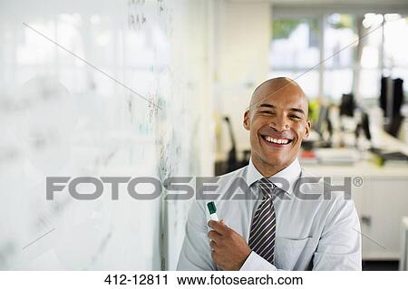 Businessman smiling at whiteboard in office View Large Photo Image Stock Image - Businessman smiling at whiteboard in office. Fotosearch