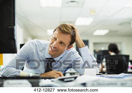 Businessman squinting at desk in office View Large Photo Image Stock Photo - Businessman squinting at desk in office. Fotosearch