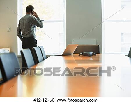 Stock Photograph - Businessman talking on cell phone in conference room. Fotosearch