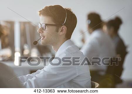 Stock Image - Businessman wearing headset in office. Fotosearch