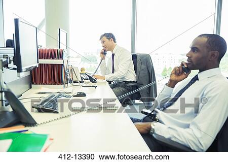 Stock Image - Businessmen talking on telephones in office. Fotosearch
