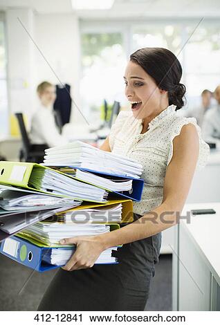 Stock Image - Businesswoman carrying folders in office. Fotosearch