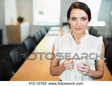 Stock Image - Businesswoman drinking cup of coffee in conference room. Fotosearch