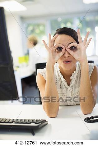 Stock Image - Businesswoman making a face at desk in office. Fotosearch
