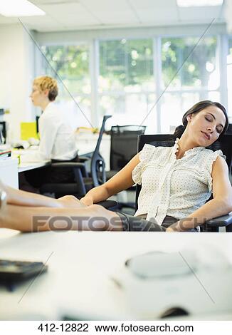 Stock Image - Businesswoman napping at desk in office. Fotosearch