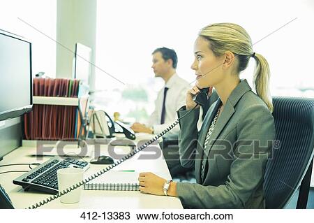 Stock Image - Businesswoman talking on telephone in office. Fotosearch