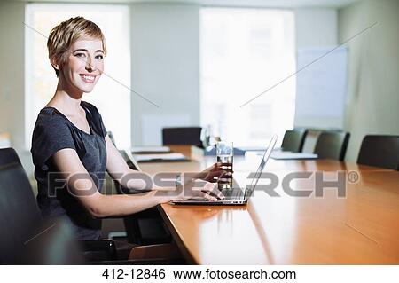 Businesswoman using laptop at conference table View Large Photo Image Stock Photograph - Businesswoman using laptop at conference table. Fotosearch