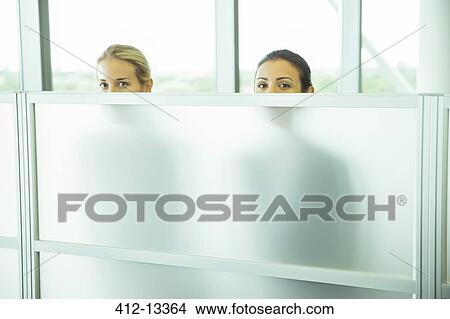 Businesswomen peeking over half wall in office View Large Photo Image Picture - Businesswomen peeking over half wall in office. Fotosearch