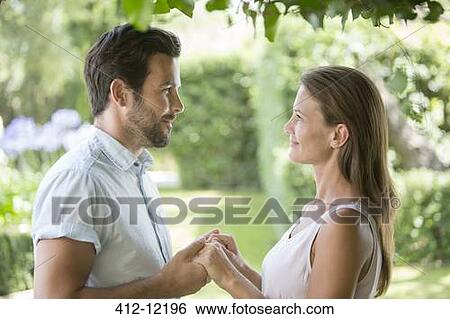 Stock Photograph - Couple holding hands face to face in garden. Fotosearch