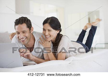 Stock Image - Couple using laptop on bed. Fotosearch