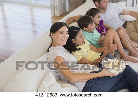 Family watching movie on sofa in living room View Large Photo Image Stock Image - Family watching movie on sofa in living room. Fotosearch