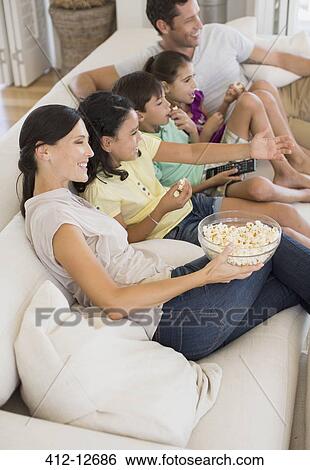 Family watching movie on sofa in living room View Large Photo Image Stock Photograph - Family watching movie on sofa in living room. Fotosearch