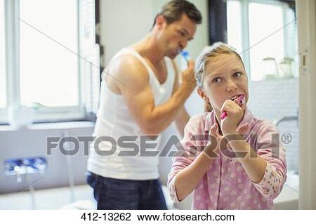 Stock Image - Father and daughter brushing teeth in bathroom. Fotosearch