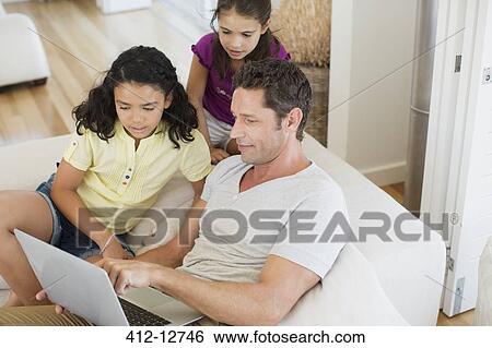 Father and daughters using laptop on sofa in living room View Large Photo Image Stock Photograph - Father and daughters using laptop on sofa in living room. Fotosearch