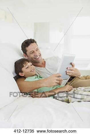 Father and son using digital tablet on bed View Large Photo Image Stock Photography - Father and son using digital tablet on bed. Fotosearch