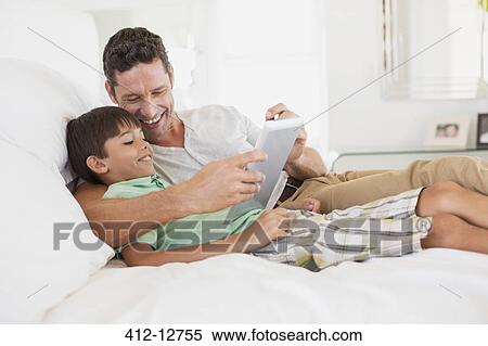 Father and son using digital tablet on bed View Large Photo Image Stock Photography - Father and son using digital tablet on bed. Fotosearch