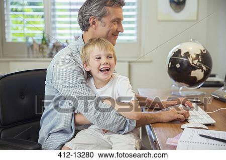 Stock Image - Father holding son and using computer. Fotosearch