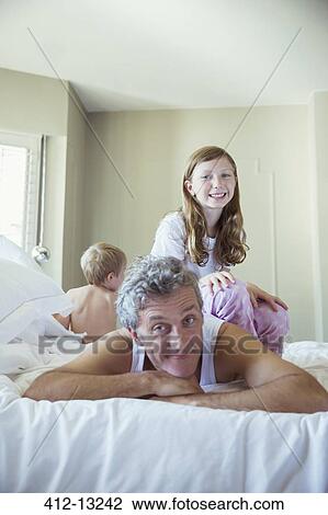 Stock Image - Father playing with children on bed. Fotosearch
