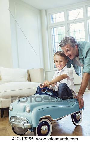 Stock Photography - Father pushing son in toy car. Fotosearch