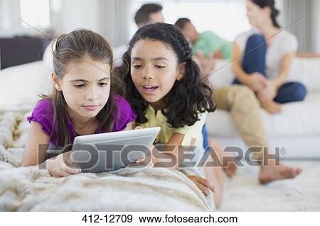 Girls using digital tablet on sofa in living room View Large Photo Image Stock Photo - Girls using digital tablet on sofa in living room. Fotosearch