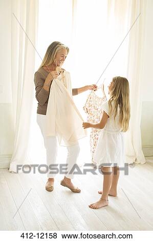 Stock Photo - Grandmother and granddaughter holding clothing at window. Fotosearch