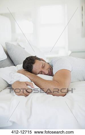 Stock Photography - Man hugging pillow on bed. Fotosearch