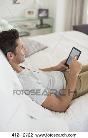 Stock Image - Man using digital tablet on bed. Fotosearch