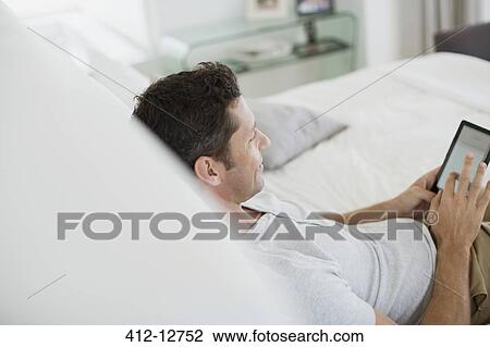 Man using digital tablet on bed View Large Photo Image Stock Image - Man using digital tablet on bed. Fotosearch
