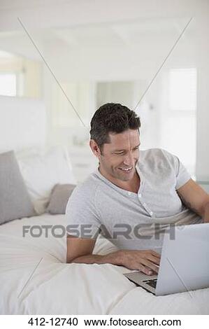 Man using laptop on bed View Large Photo Image Stock Image - Man using laptop on bed. Fotosearch