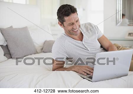 Man using laptop on bed View Large Photo Image Stock Photo - Man using laptop on bed. Fotosearch
