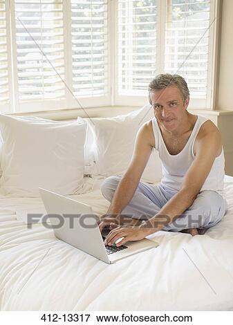 Man using laptop on bed View Large Photo Image Stock Photo - Man using laptop on bed. Fotosearch