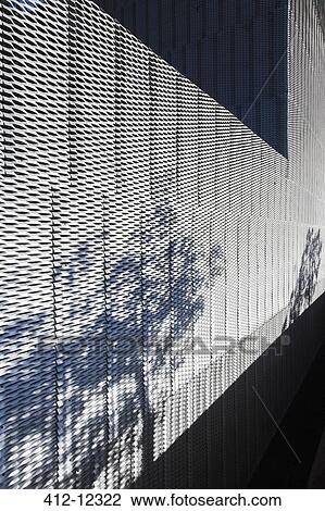 Stock Image - Plants casting shadow on textured wall of modern building. Fotosearch