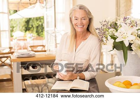 Senior woman drinking coffee and reading book in kitchen View Large Photo Image Picture - Senior woman drinking coffee and reading book in kitchen. Fotosearch
