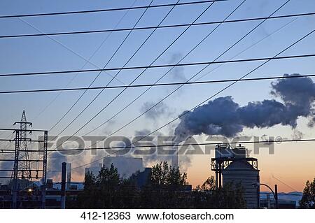 Stock Image - Silhouette of smoke emitting from factory at sunrise. Fotosearch
