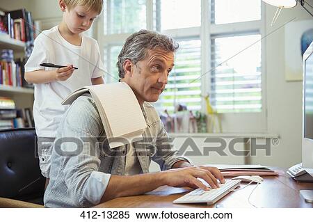 Son distracting father at work in home office View Large Photo Image Stock Photography - Son distracting father at work in home office. Fotosearch