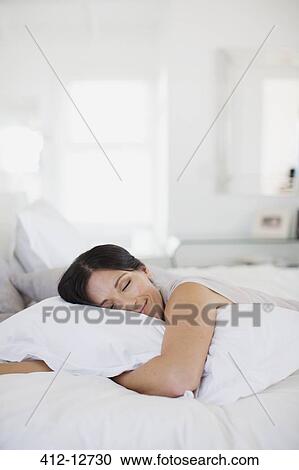 Stock Image - Woman hugging pillow on bed. Fotosearch